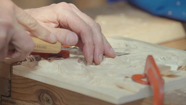 Close-up of  woodworker hands chiseling accurately a wooden table creating a design. Real time