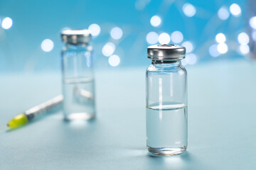 Two bottles of vaccine and syringe injection on blue background. Concept of prevention, immunization and treatment from infection. Medicine infectious concept. Close up.