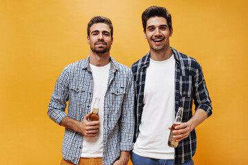 Beautiful bearded young men in white t-shirts and checkered shirts pose on orange background and...