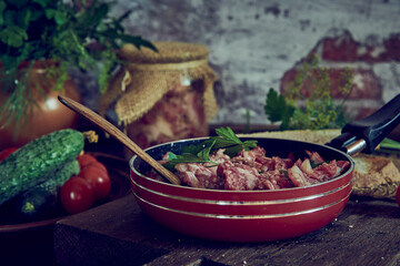 A frying pan with stewed meat seasoned with fresh herbs on a wooden countertop.