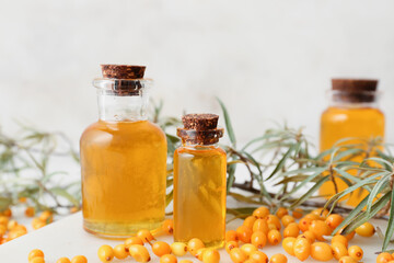 Bottles of sea buckthorn essential oil on light background