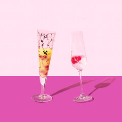 Dancing glasses posh concept. A glass of cocktail and a glass of champagne. Arrangement against purple and light pink.