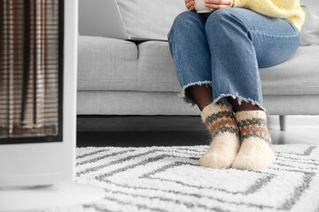 Young woman sitting near electric heater at home. Concept of heating season