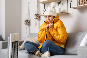 Fototapeta Young woman sitting near electric heater at home. Concept of heating season obraz