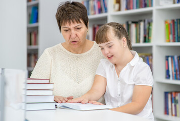 Teacher and girl with syndrome down read a book at library. Education for disabled children concept