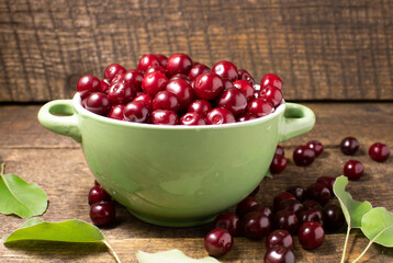 Cherry berries in a green cup on a wooden background.