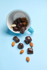 Cup with sweet chocolate candies and nuts on color background
