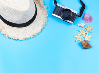 flat lay of  camera, straw hat on blue background, decorated with sea shells and starfishes, copy space. Summer beach vacation background.
