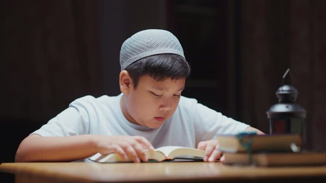 Asian Muslim son sitting and reading the Quran at his home during the month of Ramadan, 4k resolution.