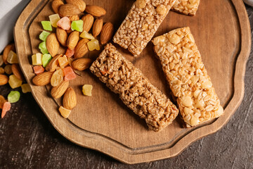 Board with healthy cereal bars, candied fruits and nuts on dark background