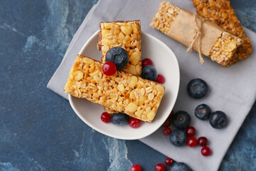 Bowl with healthy cereal bars and berries on color background