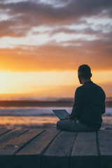 back of a sitting digital nomad remote working man on a boardwalk at the beach working with laptop during sunset
 - obrazy, fototapety, plakaty
