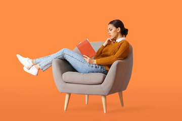 Beautiful young woman with book sitting in armchair on color background