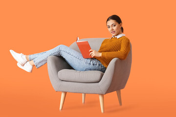 Fototapeta na wymiar Beautiful young woman with book sitting in armchair on color background