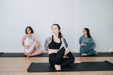 Obraz premium Calm women practicing yoga in a group, doing side twisting stretches