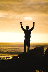 Fototapeta na wymiar happy successful MAN in YES POSE on beach rocks AT THE ocean WITH arms wide open enjoying life 