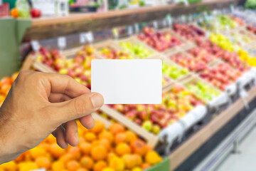 Empty plastic grocery card in hand on supermarket background. Grocery card for discounts and promotions in shops and supermarkets