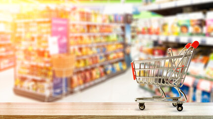 Supermarket grocery table background with cart. Food and groceries blurred on store shelves. - obrazy, fototapety, plakaty