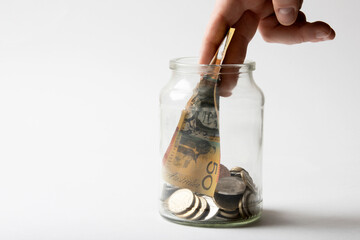 Male hand placing 50 dollar note into savings coin jar.