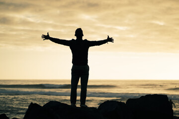 Fototapeta premium happy successful MAN in YES POSE on beach rocks AT THE ocean WITH arms wide open enjoying life 