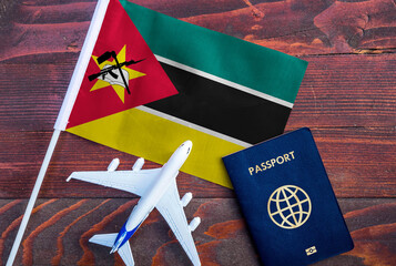 Flag of Mozambique with passport and toy airplane on wooden background. Flight travel concept
