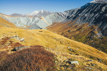 Obraz premium Awesome autumn landscape with great snow-covered mountains and sharp rockies. Spectacular colorful view to mountain ridge and yellow valley in fall. Wonderful mountain scenery in orange autumn colors.