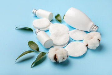 Cotton pads, flowers and bottles of cosmetic products on color background