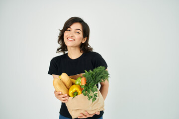 cheerful woman with a package of groceries vegetables healthy food light background