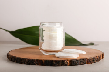 Board with cotton pads in glass jar on light background