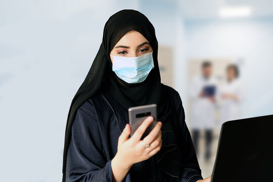 Middle Eastern Arab woman at a hospital reception wearing protective face mask and traditional Hijab Abaya. Emirati girl works at a healthcare company