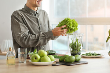 Young man preparing healthy green smoothie in kitchen