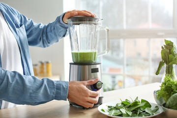 Young man preparing healthy green smoothie in kitchen