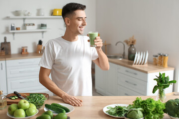 Young man drinking healthy green smoothie in kitchen