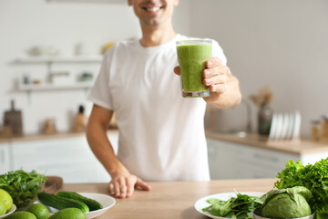 Young man with glass of healthy green smoothie in kitchen