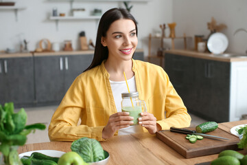 Young woman with glass of healthy green smoothie in kitchen
