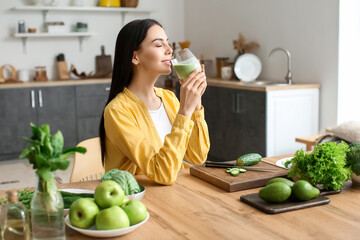 Young woman drinking healthy green smoothie in kitchen