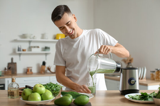 Young man pouring healthy green smoothie into glass in kitchen