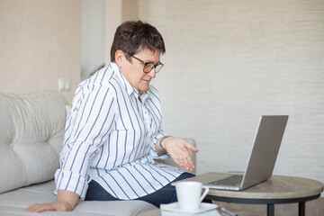 middle aged woman working by laptop and drinking coffee at home.