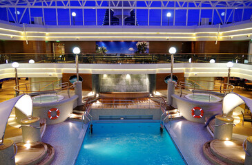 View into indoor solarium swimming pool with several decks and whirlpool and bar illuminated light...