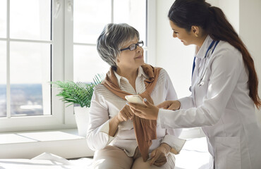 Friendly female nurse teaches an older woman to use modern health programs on her mobile phone....