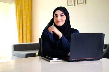 Arab woman at home with laptop wearing traditional Hijab worn by Middle Eastern women as part of the culture. Emirati lady wearing full covering clothing Abaya ideal for business corporate concept