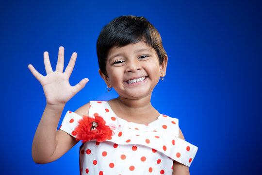Cute little girl kid saying hi anf how are how by looking at camera on blue color background - concept of child greeting.