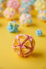 Set of multicolor handmade modular origami balls or Kusudama Isolated on yellow background. Visual art, geometry, art of paper folding, paper crafts. Close up, selective focus, copy space.