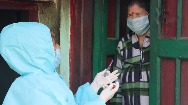 Young woman doctor in PPE protective mask and gloves holding a syringe and coronavirus vaccine, standing with village women explaining importance of corona virus vaccine. The concept of a new vaccine 