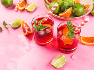 Refreshing summer red cocktail in glasses with blood orange and lime on pink background with mint