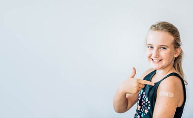 Happy girl giving thumb up and showing her arm with bandage after got vaccinated, child immunization, covid delta vaccine