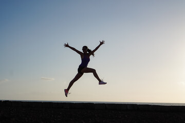 silhouette of a successful  jumping and  joyful woman on beach boardwalk during sunset or sunrise for motivation