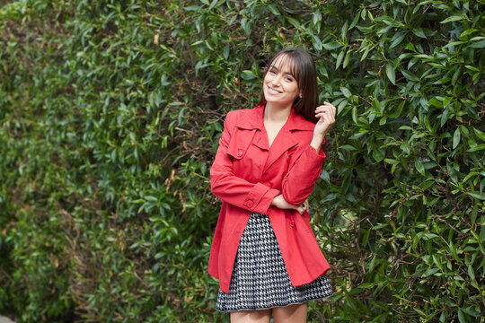 Smiling young woman in red jacket standing in park