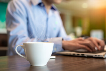 Blurred of cup of hot coffee with businessman use computer