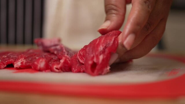 Taking fresh, raw, juicy slices of beef steak and cutting them into cubes - slow motion isolated close up